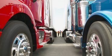 Truck drivers talking while standing between Class 8 trucks and trailers in a parking lot.